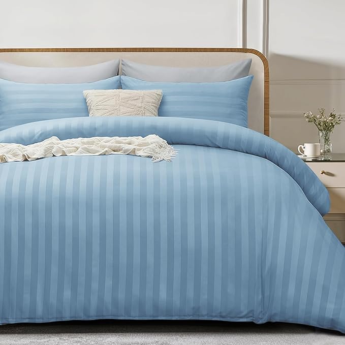 Blue striped bedding set on a bed with pillows and a side table in the background.